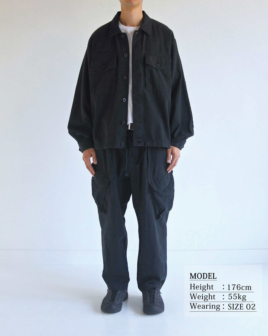 ミリタリーのシャツジャケットを現代的シルエットに更新。裾のドローコードで着丈のニュアンスを自在に調整可能です。素材には、やや甘織りで肌馴染みの良い10sヘリンボンを採用。ストーンバイオウォッシュを施すことで、クラシカルな生地感に柔らかな風合いとこなれ感をプラスした、着回し力の高い一着に仕上げました。

A modern update to the classic military shirt jacket, featuring hem drawcords for an adjustable silhouette. Crafted from 10s herringbone, slightly loose-knitted for a soft, comfortable touch. This BLACK piece has been treated with a stone bio-wash, giving the traditional weave a natural, worn-in texture and a sophisticated casual feel.