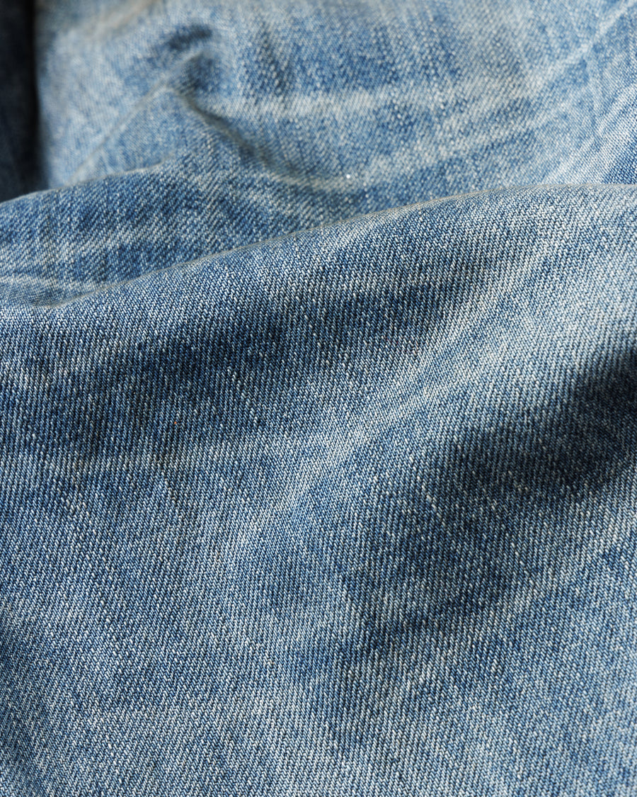 1985年のLEVIS 550をベースに再構築した、ワイドテーパードのリメイク5Pデニム。
12.5ozデニムのタテ糸には中白のインディゴロープ染色糸を使用し、ムラ感のある豊かな表情を演出。タテ落ちとインディゴの濃淡を活かすことで、ヴィンテージにはない独自の風合いを表現しています。さらに手作業のトーンコントロールと特別なエイジング加工を加えることで奥行きある仕上がりに。オリジナル染料の吹き付けにより、モダンでソリッドな印象も併せ持つ一本です。This remade 5P denim features a wide tapered silhouette inspired by the 1985 LEVIS 550.
The 12.5oz denim uses medium-white indigo rope–dyed warp yarns, giving it a textured, slubby character.
By highlighting vertical fading and vivid indigo variations, it achieves a look distinct from vin