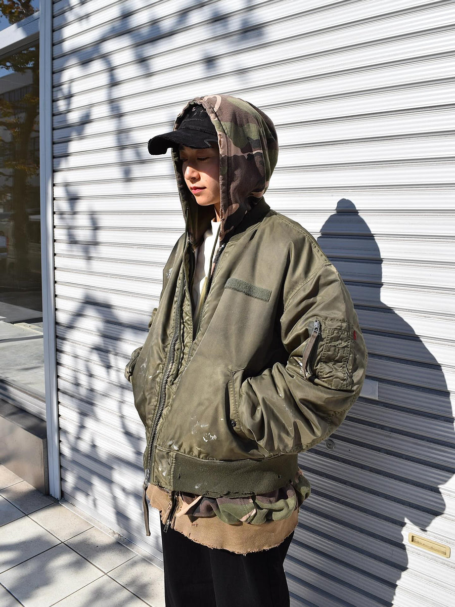 忠実なディテールを保ちながら、シルエットを現代的に整えたMA-1ジャケット。加工によりヴィンテージの風合いを再現した一着です。肉厚でミリタリーらしいツイル生地を使用し、打ち込みの密度や肌触りまでビンテージMA-1に近い仕上がりに。さらに、ダートペイントや特殊吹き付け、ダメージ加工を重ね、洗いをかけて染料を自然に剥がすことで、深みのある表情を生み出しています。カラーはオリーブ。