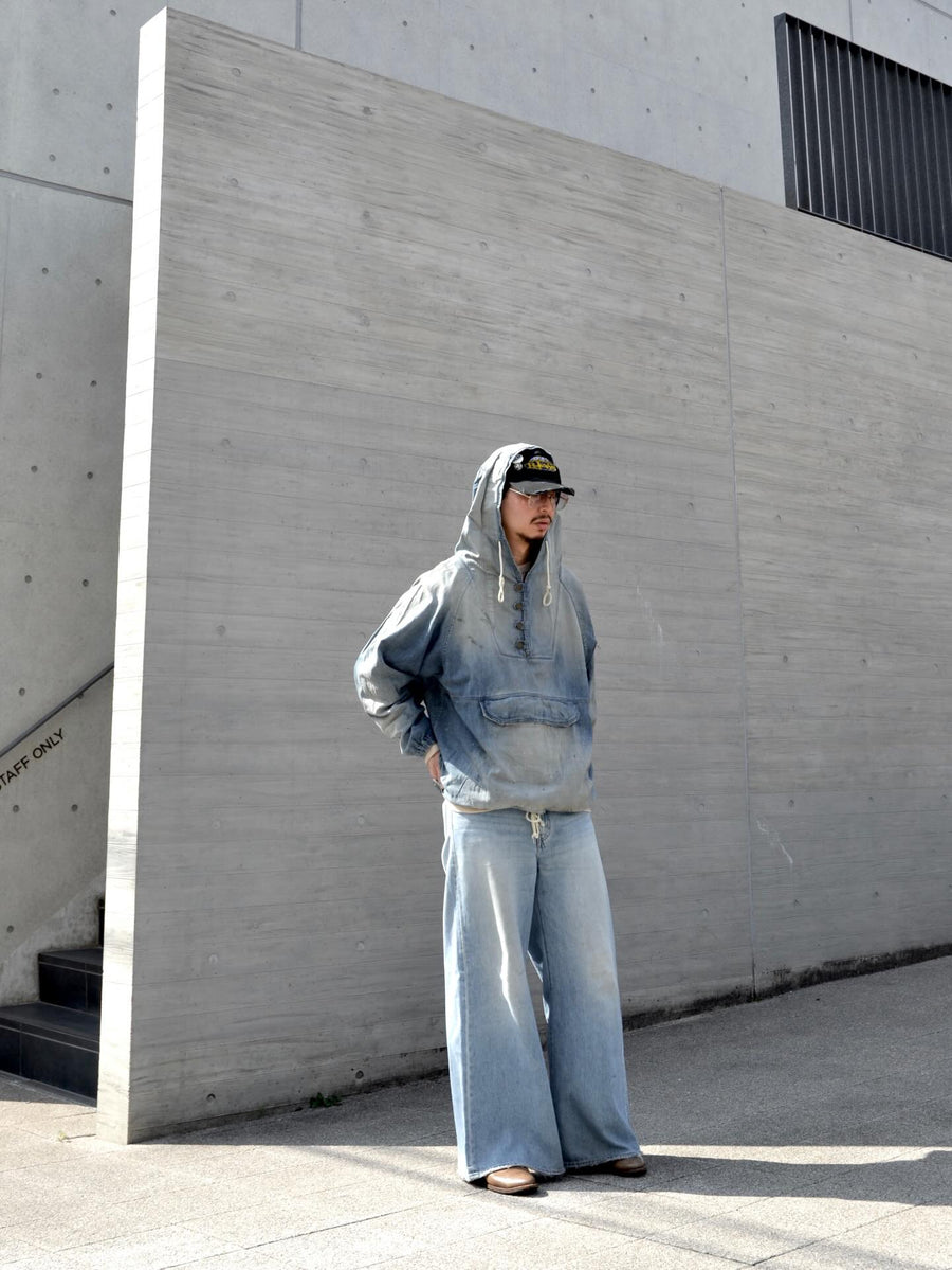 フード口のボタンの開閉により、首まわりのニュアンスを変えて楽しめる一着。素材には、経糸にコットンムラ糸、緯糸に綿麻混紡糸を使用した綿麻6ozデニムを採用しました。シャープなムラ感とリネン混ならではの粗野な風合いが、ヴィンテージの魅力を引き立てます。エイジング加工を施すことで、全体にリアリティのあるアタリ感を出し、長年着込んだような深みのある表情に仕上げました。A versatile piece featuring adjustable hood buttons to create a clean or relaxed neckline. Crafted from 6oz cotton-linen denim, the fabric combines sharp slub textures with a rustic linen feel for an authentic vintage character. Treated with an aging process to create realistic wear and fade, this INDIGO garment offers a sophisti