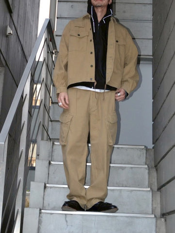 ミリタリートラウザーズをベースに、シルエットを現代的にリファイン。印象的な斜めのカーゴポケットが、立体感と実用性を両立させています。裾にかけて緩やかに絞られたテーパードラインにより、無骨ながらも洗練された印象に。素材には肌馴染みの良い10sヘリンボンを採用し、ストーンバイオウォッシュで柔らかな風合いとこなれ感を引き出しました。

Military trousers refined with a modern tapered silhouette. The distinctive slanted cargo pockets offer both practical utility and a structured look. Crafted from soft, classic 10s herringbone, this KHAKI pair has been treated with a stone bio-wash, providing a comfortable, worn-in texture and a sophisticated take on rugged style.