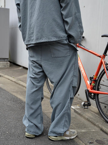 ポリエステル100％ながら、綿のような質感と軽量性を備えた高機能素材を採用。タスラン加工糸によるポリエステルオックスは、シワになりにくく速乾性にも優れています。染色が困難なポリエステルに特殊顔料染めを施すことで、化繊特有の光沢を抑え、ナチュラルで奥行きのある絶妙なフェード感と落ち着いた表情を実現しました。

High-performance polyester oxford with a cotton-like touch, offering quick-dry and wrinkle-resistant benefits. This GRAY BLUE item features a special pigment dye—a rare process for polyester—achieving a sophisticated, faded texture and a matte finish that perfectly balances technical utility with a natural, lived-in aesthetic.