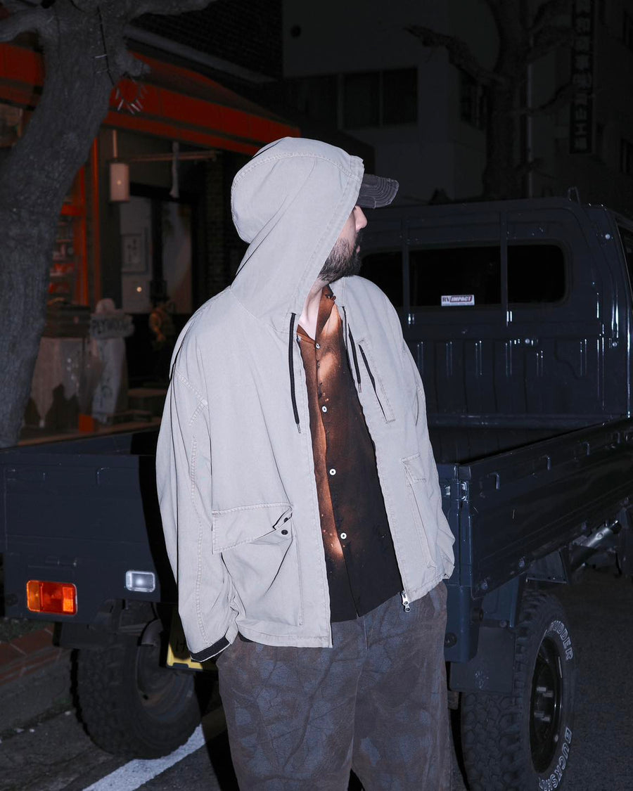 ポリエステル100％でありながら、綿のような質感と軽量性を備えた高機能な一着。タスラン加工糸を使用したポリエステルオックスを採用し、シワになりにくく速乾性に優れたイージーケア性を実現しました。本来染色が困難な素材に特殊顔料染めを施すことで、化繊特有の光沢を抑えた、ナチュラルで奥行きのある絶妙なフェード感を表現しています。

A high-performance piece crafted from polyester oxford, offering a cotton-like touch with lightweight, quick-dry, and wrinkle-resistant properties. This GRAY BEIGE item features a special pigment dye—a rare process for polyester—achieving a sophisticated, faded texture and a matte finish that defies its synthetic origins.