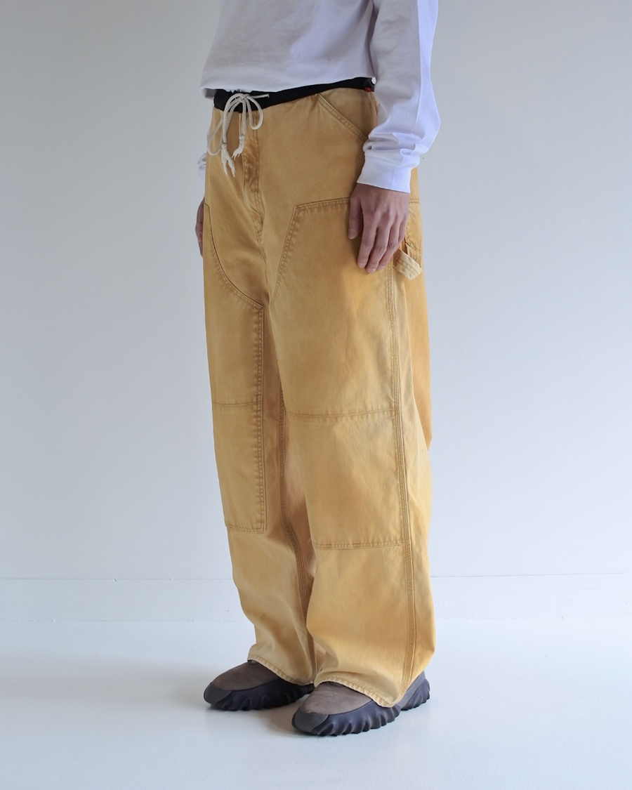 【 商品名：ダブルニーダックペインターパンツ 】

本製品は、レングスをやや長めに設定したイエローカラーのペインターパンツです。ウエスト部分にはナイロンオックス生地で切り替えを施し、ワーク感を抑えたデザインに仕上げています。生地には頒布の中でも最も薄手の11号帆布生地を使用しており、強度・耐久性に優れるだけでなく、着用を重ねるごとにアタリなどの経年変化を楽しめる素材です。また、水や薬品の使用量を抑えつつ生地の凹凸部分のアタリを強調し、同時に自然な脱色感を生み出す特殊エイジング加工を施しています。