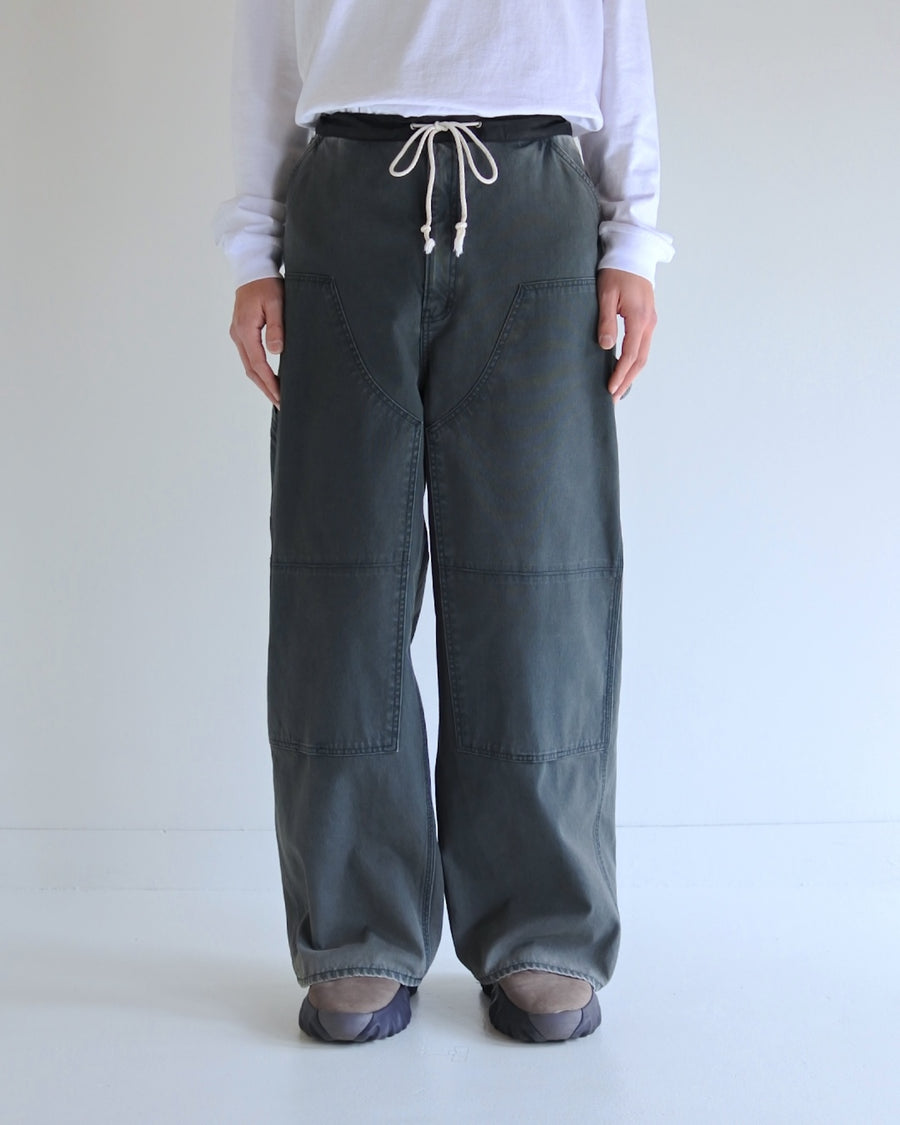 【 商品名：ダブルニーダックペインターパンツ 】

本製品は、レングスをやや長めに設定したブラックカラーのペインターパンツです。ウエスト部分にはナイロンオックス生地で切り替えを施し、ワーク感を抑えた上品なデザインに仕上げています。生地には頒布の中でも最も薄手の11号帆布生地を採用しており、強度・耐久性に優れるとともに、着用を重ねるごとにアタリなどの経年変化を楽しめる素材です。また、水や薬品の使用量を抑えながら生地の凹凸部分のアタリを強調し、同時に自然な脱色感を加える特殊エイジング加工を施しています。