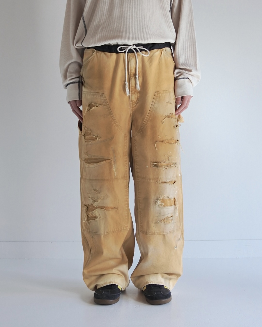 【 商品名：リメイクダブルニーダックペインターパンツ 】

本製品は、レングスをやや長めに設定したイエローカラーのペインターパンツです。ウエスト部分にはナイロンオックス生地で切り替えを施し、ワーク感を抑えたバランスの良いデザインに仕上げています。生地には頒布の中でも最も薄手の11号帆布生地を使用しており、強度・耐久性に優れるだけでなく、着用を重ねるごとにアタリなどの経年変化を味わえる素材です。また、水や薬品の使用量を抑えながら生地の凹凸部分のアタリを強調し、同時に自然な脱色感を与える特殊エイジング加工に加え、サンフェードによるダメージ加工も施すことで、より深みのある表情に仕上げています。