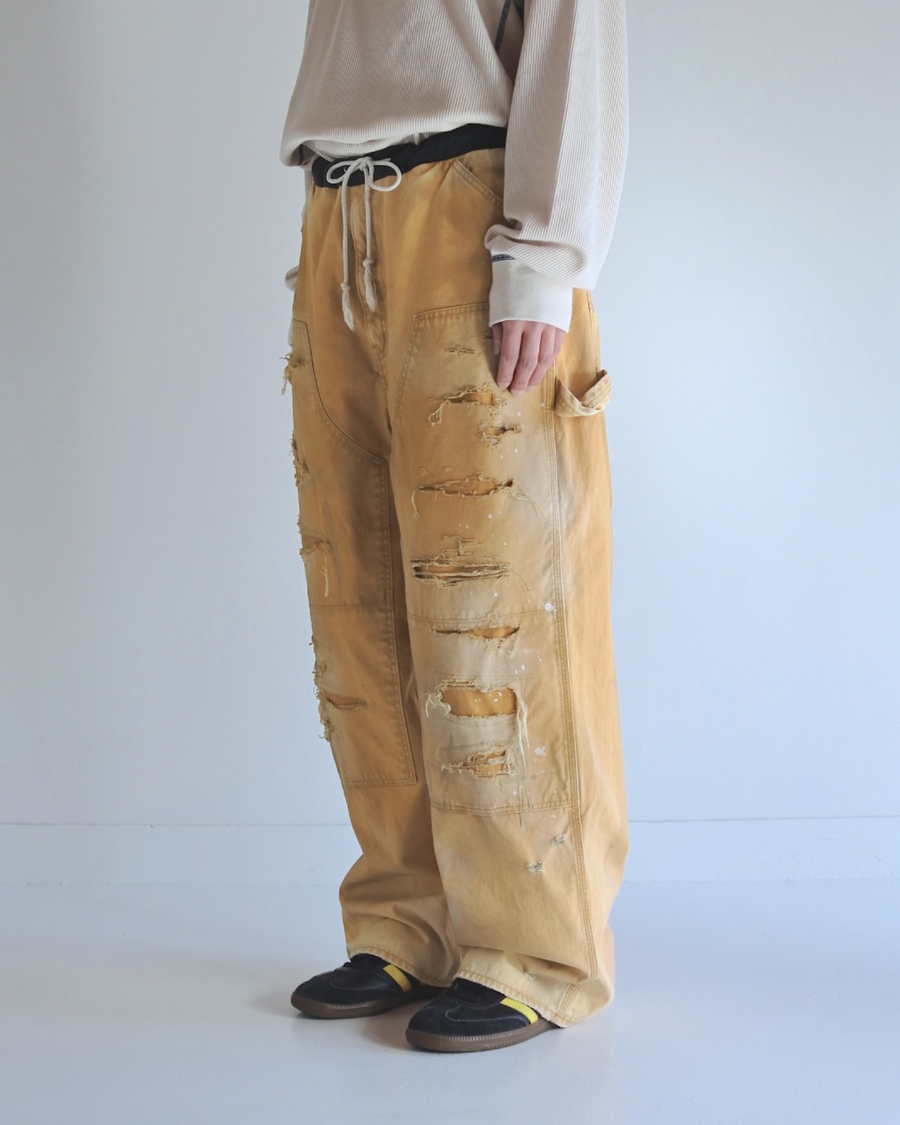 【 商品名：リメイクダブルニーダックペインターパンツ 】

本製品は、レングスをやや長めに設定したイエローカラーのペインターパンツです。ウエスト部分にはナイロンオックス生地で切り替えを施し、ワーク感を抑えたバランスの良いデザインに仕上げています。生地には頒布の中でも最も薄手の11号帆布生地を使用しており、強度・耐久性に優れるだけでなく、着用を重ねるごとにアタリなどの経年変化を味わえる素材です。また、水や薬品の使用量を抑えながら生地の凹凸部分のアタリを強調し、同時に自然な脱色感を与える特殊エイジング加工に加え、サンフェードによるダメージ加工も施すことで、より深みのある表情に仕上げています。