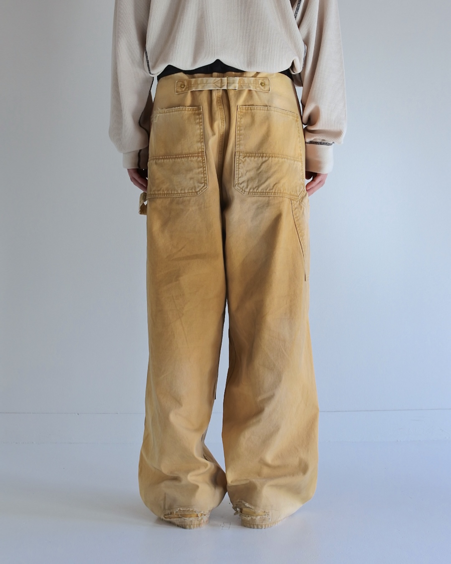 【 商品名：リメイクダブルニーダックペインターパンツ 】

本製品は、レングスをやや長めに設定したイエローカラーのペインターパンツです。ウエスト部分にはナイロンオックス生地で切り替えを施し、ワーク感を抑えたバランスの良いデザインに仕上げています。生地には頒布の中でも最も薄手の11号帆布生地を使用しており、強度・耐久性に優れるだけでなく、着用を重ねるごとにアタリなどの経年変化を味わえる素材です。また、水や薬品の使用量を抑えながら生地の凹凸部分のアタリを強調し、同時に自然な脱色感を与える特殊エイジング加工に加え、サンフェードによるダメージ加工も施すことで、より深みのある表情に仕上げています。
