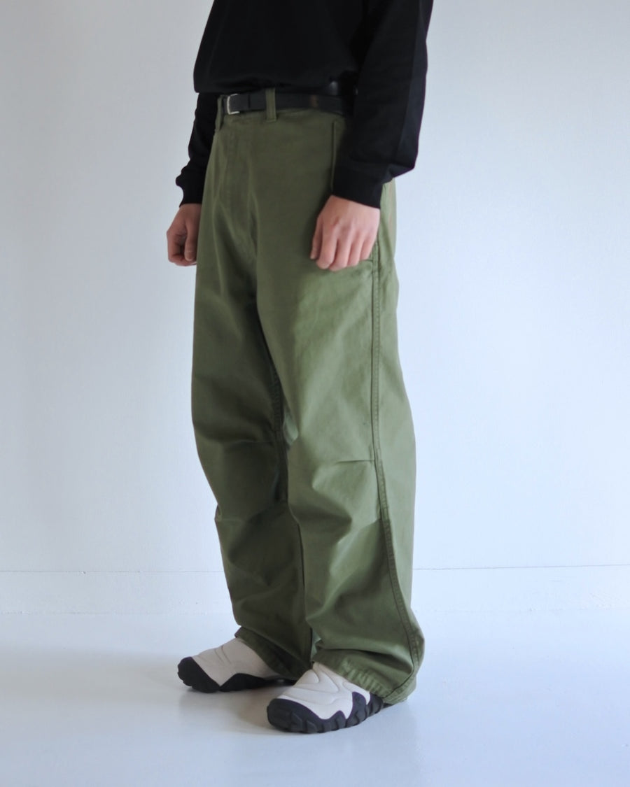 フラップポケットや膝のタック、裾のドローコードなど、ミリタリーディテールを随所に取り入れた1本。通常は内側に配置されるポケットをあえて外側に設けたカーゴポケットが印象的です。ムラ糸で織り上げたバックサテン生地は、独特のハリとコシを持ち、深みのあるオリーブカラーが魅力です。