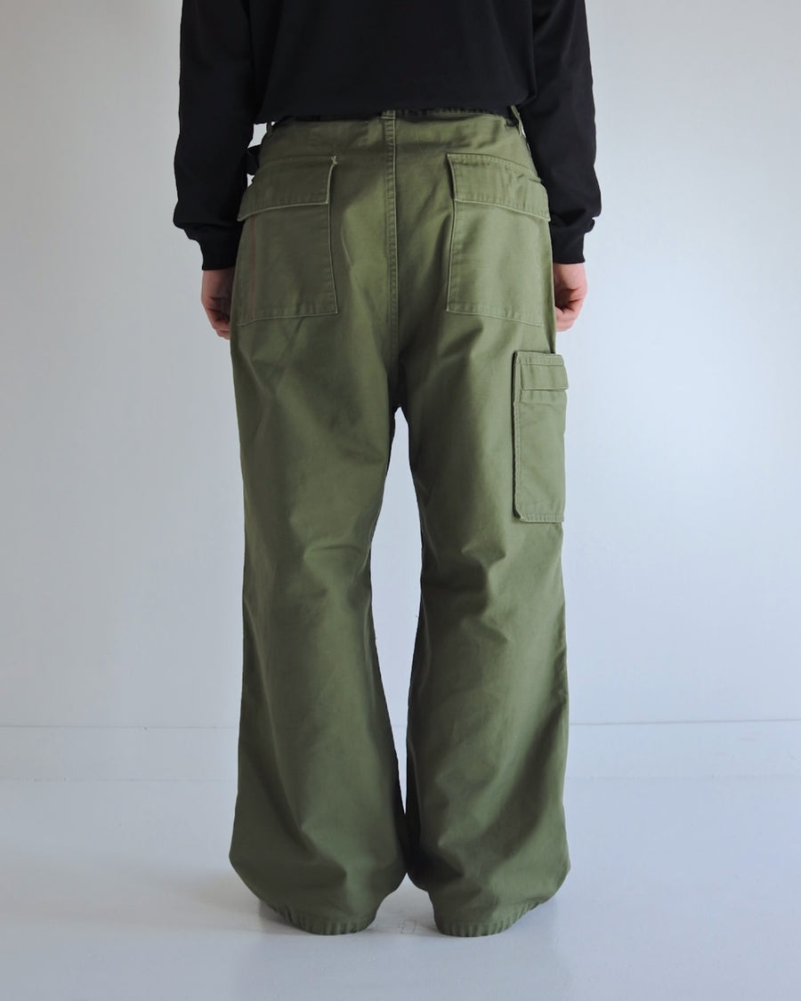 フラップポケットや膝のタック、裾のドローコードなど、ミリタリーディテールを随所に取り入れた1本。通常は内側に配置されるポケットをあえて外側に設けたカーゴポケットが印象的です。ムラ糸で織り上げたバックサテン生地は、独特のハリとコシを持ち、深みのあるオリーブカラーが魅力です。