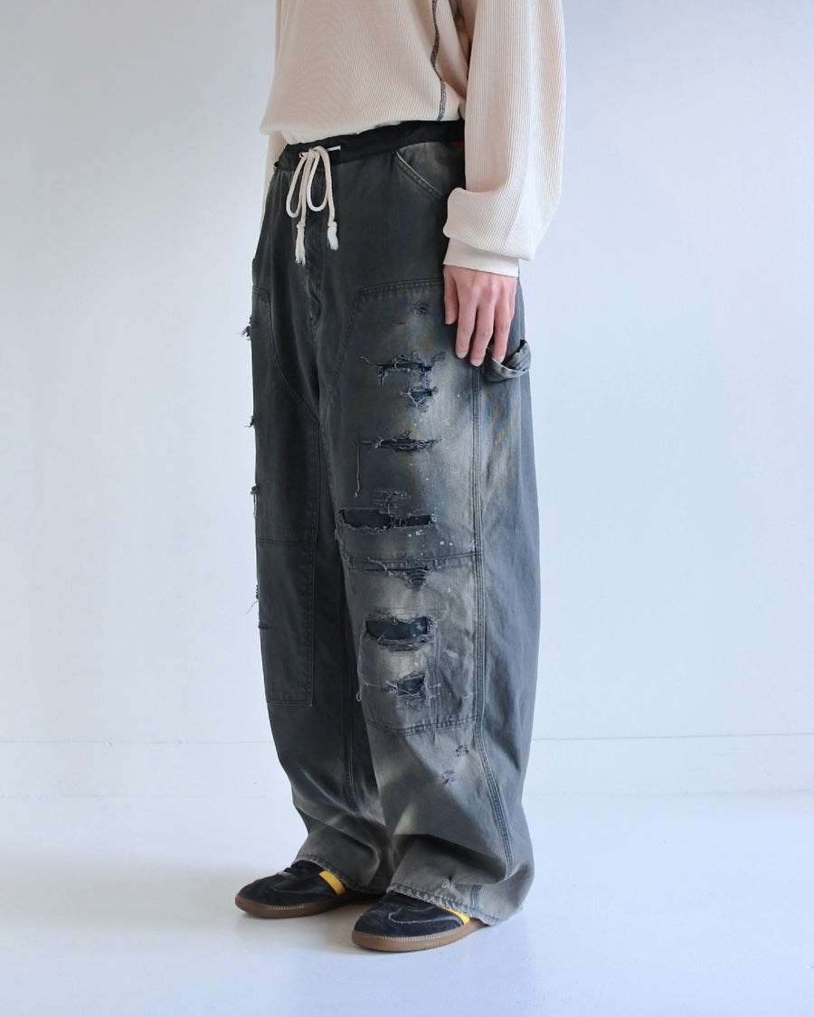 【 商品名：リメイクダブルニーダックペインターパンツ 】

本製品は、レングスをやや長めに設定したブラックカラーのペインターパンツです。ウエスト部分にはナイロンオックス生地で切り替えを施し、ワーク感を抑えつつバランスの良いデザインに仕上げています。生地には頒布の中でも最も薄手の11号帆布生地を使用しており、強度・耐久性に優れるだけでなく、着用を重ねるごとにアタリなどの経年変化を楽しめる素材です。また、水や薬品の使用量を抑えながら生地の凹凸部分のアタリを強調し、同時に自然な脱色感を与える特殊エイジング加工に加え、サンフェードによるダメージ加工も施すことで、より味わい深い表情に仕上げています。