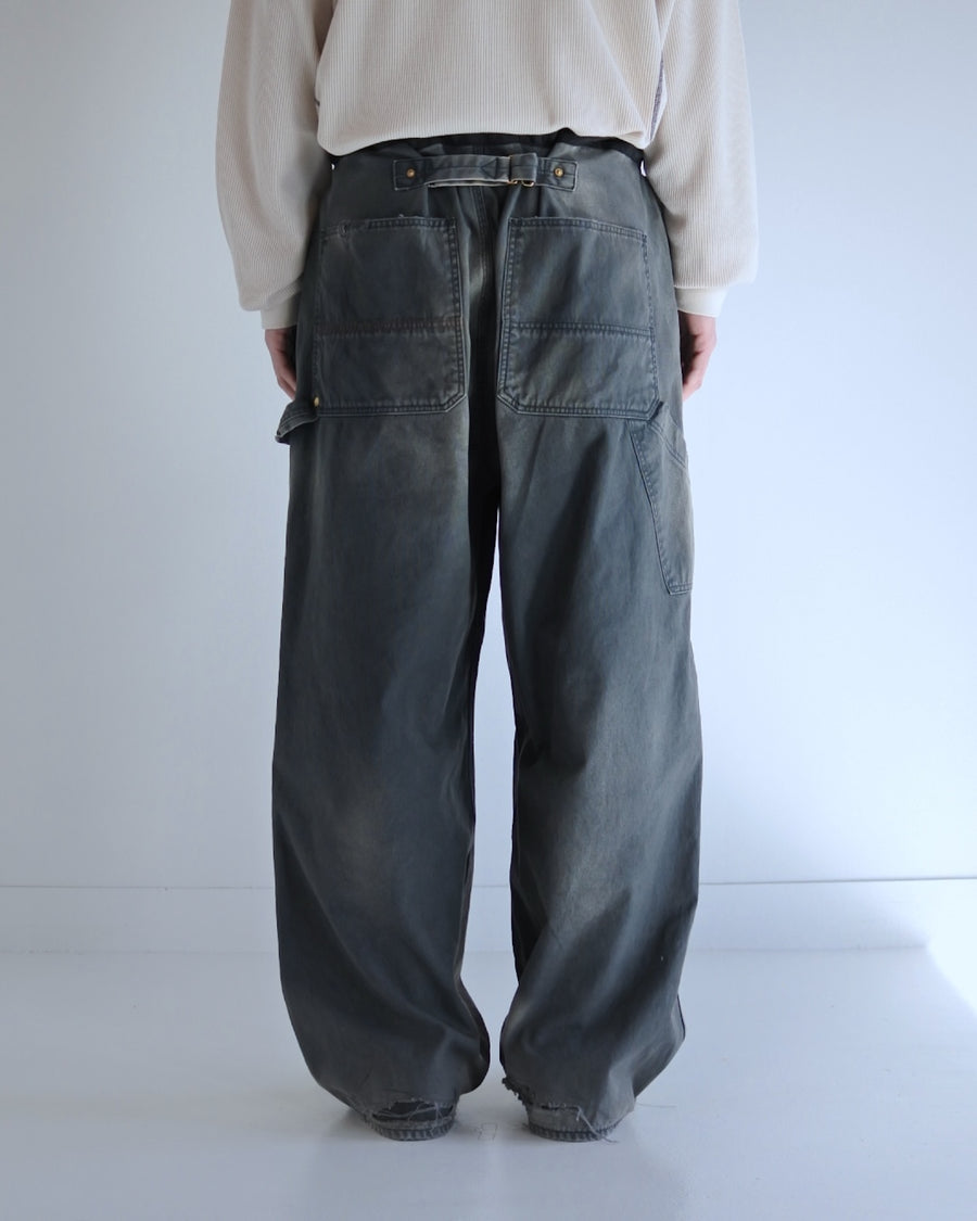 【 商品名：リメイクダブルニーダックペインターパンツ 】

本製品は、レングスをやや長めに設定したブラックカラーのペインターパンツです。ウエスト部分にはナイロンオックス生地で切り替えを施し、ワーク感を抑えつつバランスの良いデザインに仕上げています。生地には頒布の中でも最も薄手の11号帆布生地を使用しており、強度・耐久性に優れるだけでなく、着用を重ねるごとにアタリなどの経年変化を楽しめる素材です。また、水や薬品の使用量を抑えながら生地の凹凸部分のアタリを強調し、同時に自然な脱色感を与える特殊エイジング加工に加え、サンフェードによるダメージ加工も施すことで、より味わい深い表情に仕上げています。