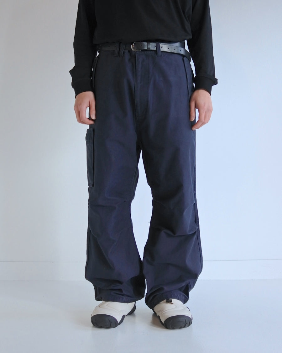 フラップポケットや膝のタック、裾のドローコードなど、ミリタリーディテールを随所に取り入れた1本。通常は内側に配置されるポケットをあえて外側に設けたカーゴポケットが印象的です。ムラ糸で織り上げたバックサテン生地は、独特のハリとコシを持ち、深みのあるネイビーカラーが魅力です。