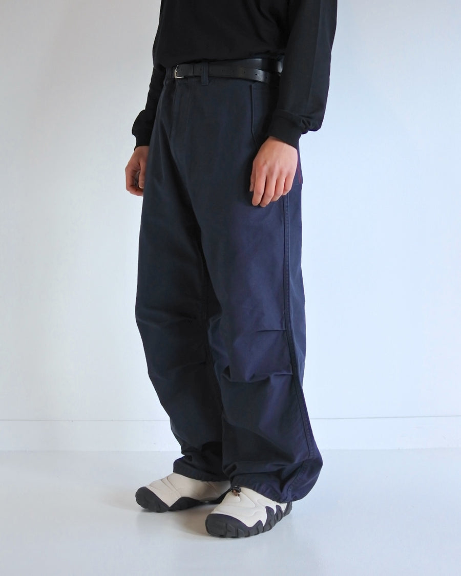 フラップポケットや膝のタック、裾のドローコードなど、ミリタリーディテールを随所に取り入れた1本。通常は内側に配置されるポケットをあえて外側に設けたカーゴポケットが印象的です。ムラ糸で織り上げたバックサテン生地は、独特のハリとコシを持ち、深みのあるネイビーカラーが魅力です。