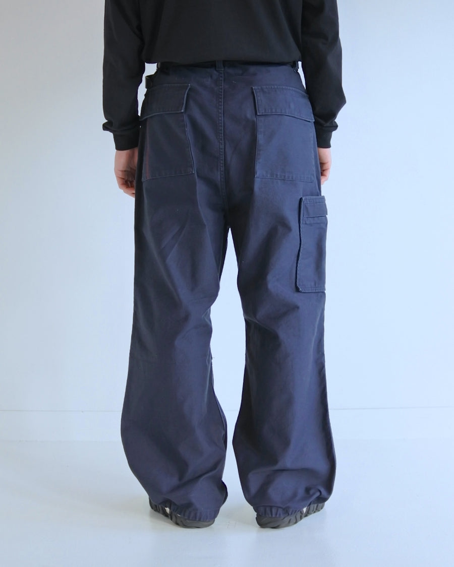 フラップポケットや膝のタック、裾のドローコードなど、ミリタリーディテールを随所に取り入れた1本。通常は内側に配置されるポケットをあえて外側に設けたカーゴポケットが印象的です。ムラ糸で織り上げたバックサテン生地は、独特のハリとコシを持ち、深みのあるネイビーカラーが魅力です。