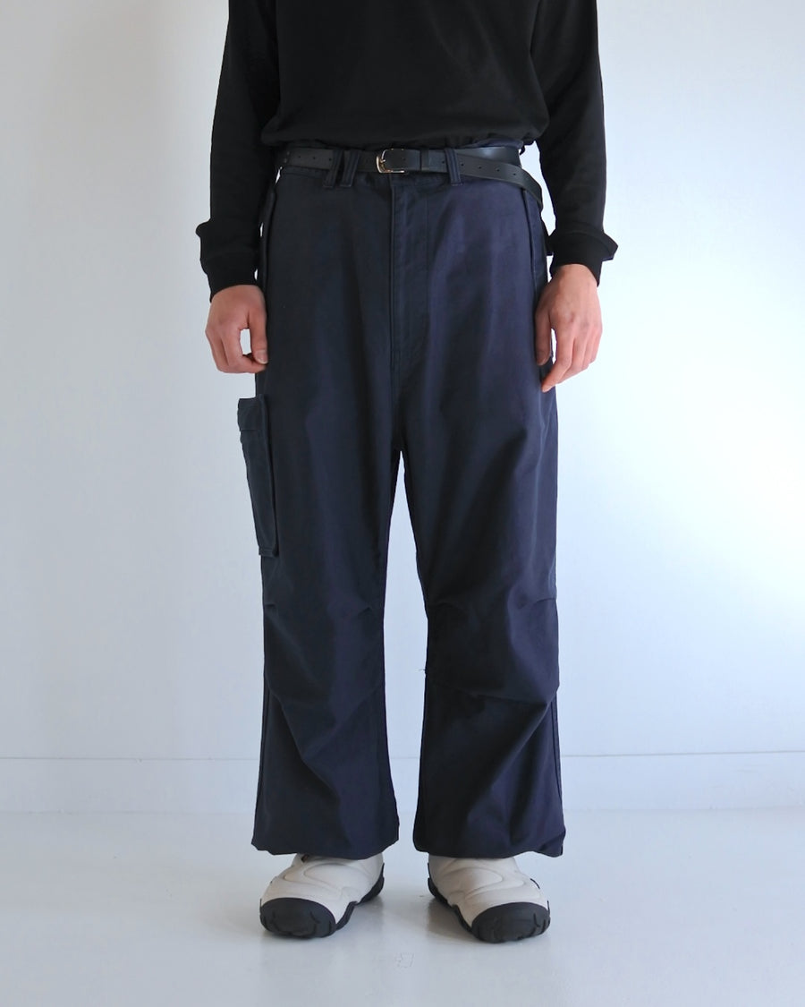 フラップポケットや膝のタック、裾のドローコードなど、ミリタリーディテールを随所に取り入れた1本。通常は内側に配置されるポケットをあえて外側に設けたカーゴポケットが印象的です。ムラ糸で織り上げたバックサテン生地は、独特のハリとコシを持ち、深みのあるネイビーカラーが魅力です。