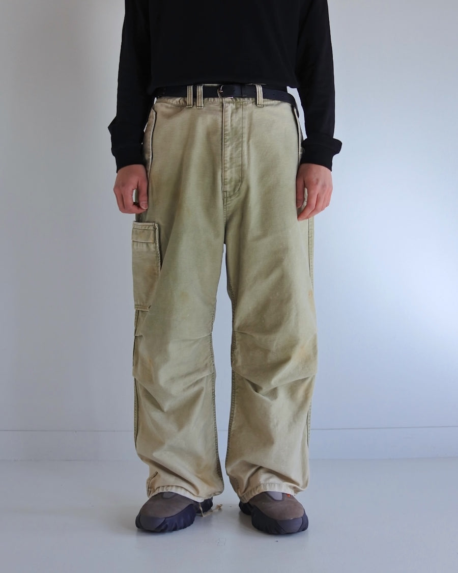 フラップポケットや膝のタック、裾のドローコードなど、ミリタリーのディテールをふんだんに取り入れた一本。内側に配置されることの多いポケットをあえて外側に設けたカーゴポケットが特徴です。ムラ糸で織り上げたバックサテン生地は、ハリとコシのある質感が魅力。さらに、水や薬品の使用を抑えながら生地の凹凸を際立たせる特殊エイジング加工を施し、深みのあるオリーブカラーに仕上げています。