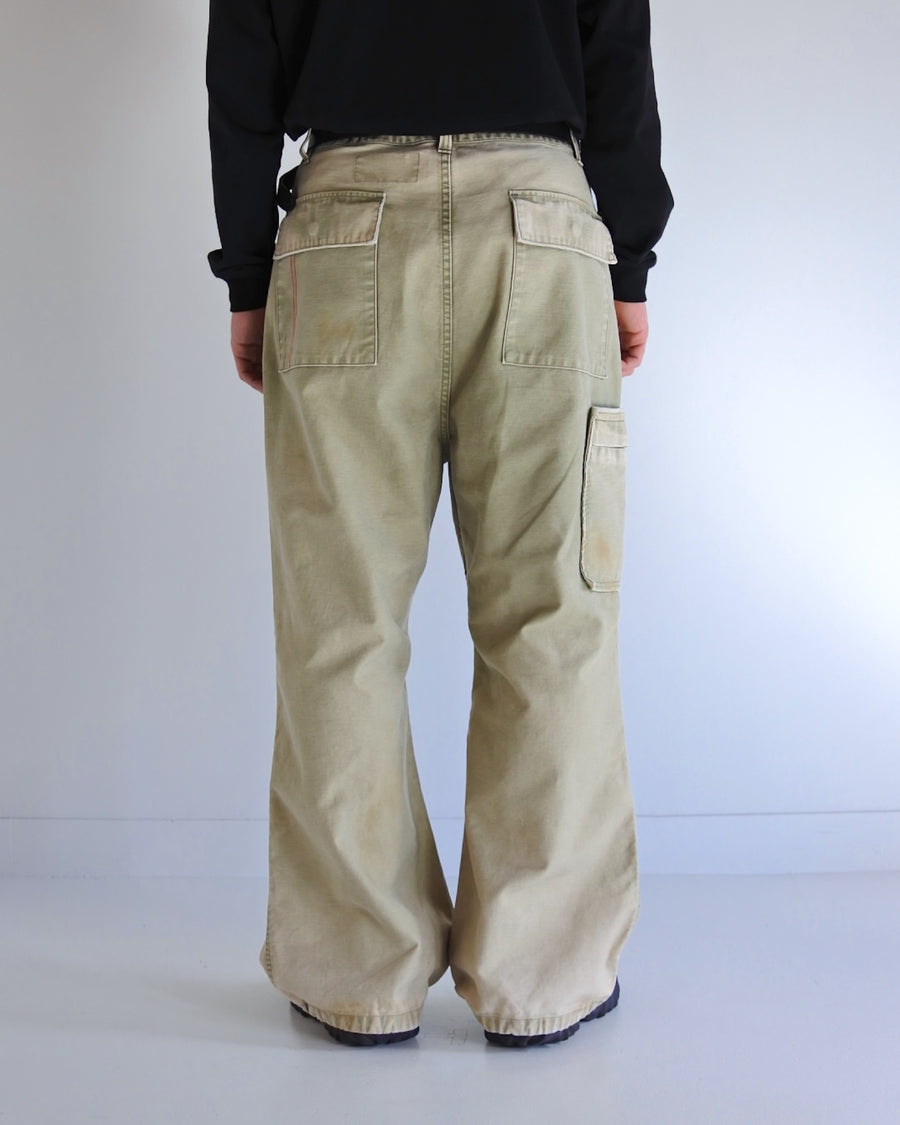 フラップポケットや膝のタック、裾のドローコードなど、ミリタリーのディテールをふんだんに取り入れた一本。内側に配置されることの多いポケットをあえて外側に設けたカーゴポケットが特徴です。ムラ糸で織り上げたバックサテン生地は、ハリとコシのある質感が魅力。さらに、水や薬品の使用を抑えながら生地の凹凸を際立たせる特殊エイジング加工を施し、深みのあるオリーブカラーに仕上げています。