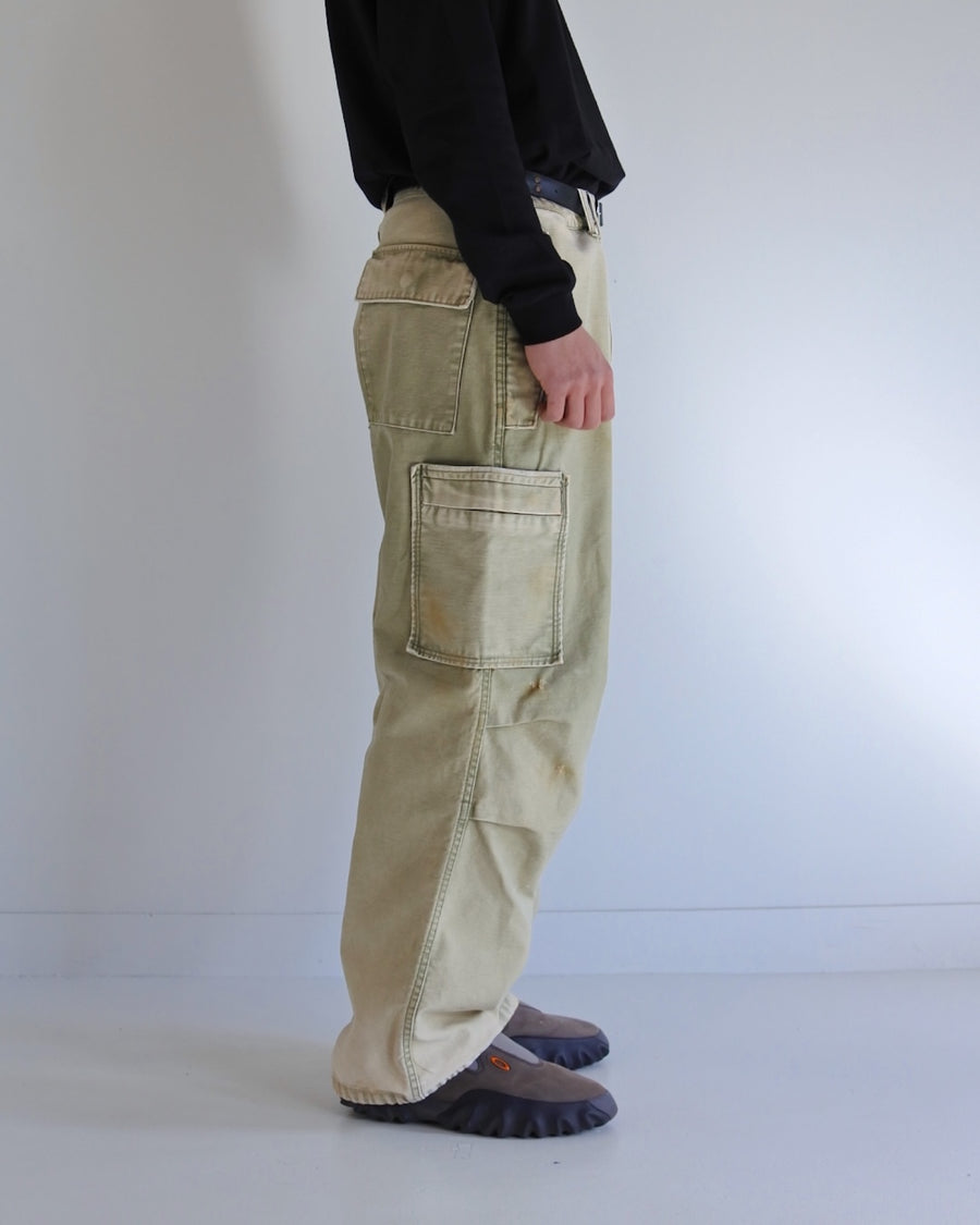 フラップポケットや膝のタック、裾のドローコードなど、ミリタリーのディテールをふんだんに取り入れた一本。内側に配置されることの多いポケットをあえて外側に設けたカーゴポケットが特徴です。ムラ糸で織り上げたバックサテン生地は、ハリとコシのある質感が魅力。さらに、水や薬品の使用を抑えながら生地の凹凸を際立たせる特殊エイジング加工を施し、深みのあるオリーブカラーに仕上げています。