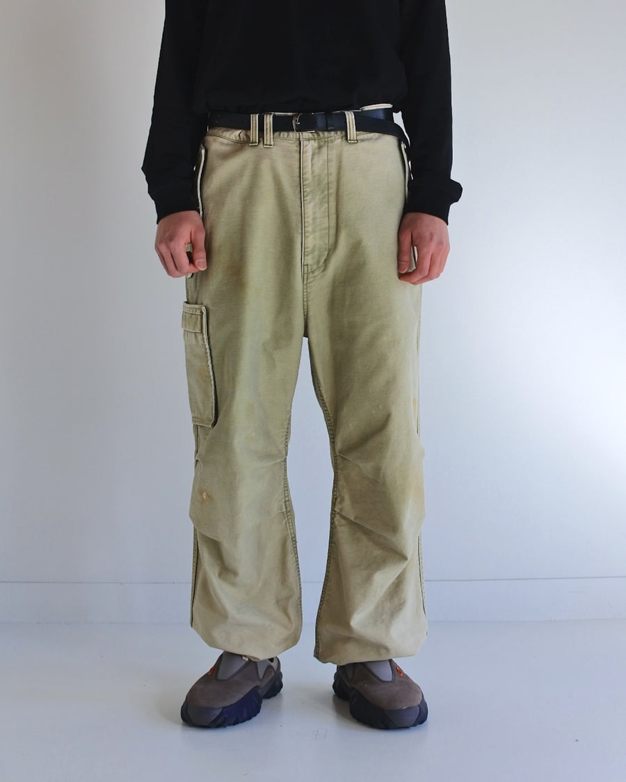 フラップポケットや膝のタック、裾のドローコードなど、ミリタリーのディテールをふんだんに取り入れた一本。内側に配置されることの多いポケットをあえて外側に設けたカーゴポケットが特徴です。ムラ糸で織り上げたバックサテン生地は、ハリとコシのある質感が魅力。さらに、水や薬品の使用を抑えながら生地の凹凸を際立たせる特殊エイジング加工を施し、深みのあるオリーブカラーに仕上げています。