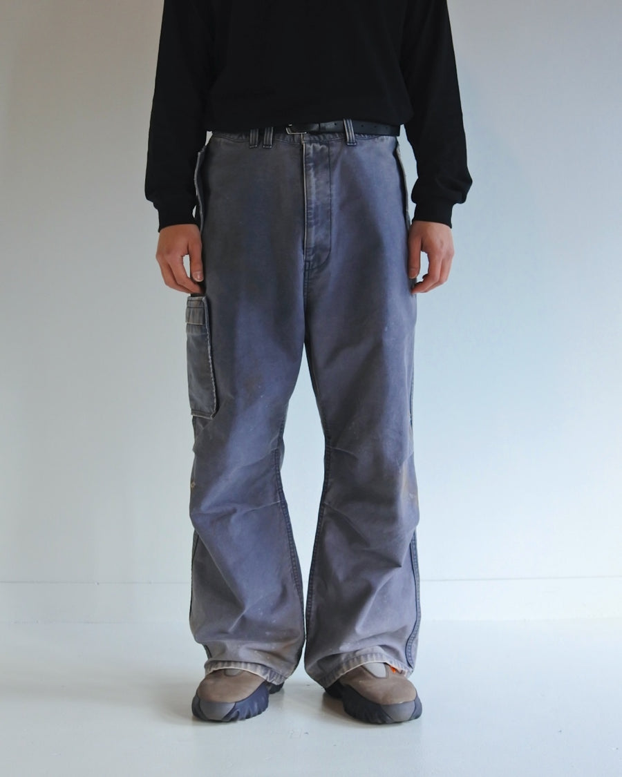 フラップポケットや膝のタック、裾のドローコードなど、ミリタリーのディテールをふんだんに取り入れた一本。内側に配置されることの多いポケットをあえて外側に設けたカーゴポケットが特徴です。ムラ糸で織り上げたバックサテン生地は、ハリとコシのある質感が魅力。さらに、水や薬品の使用を抑えながら生地の凹凸を際立たせる特殊エイジング加工を施し、深みのあるネイビーカラーに仕上げています。