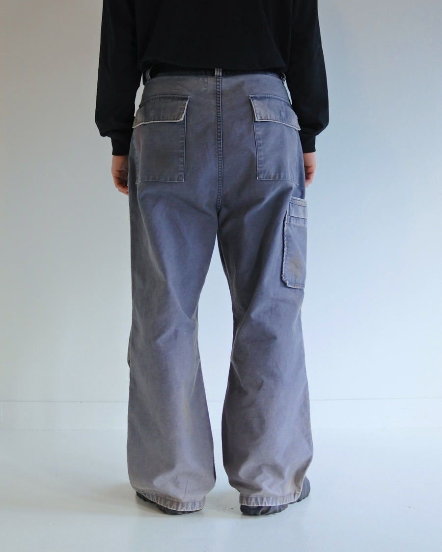 フラップポケットや膝のタック、裾のドローコードなど、ミリタリーのディテールをふんだんに取り入れた一本。内側に配置されることの多いポケットをあえて外側に設けたカーゴポケットが特徴です。ムラ糸で織り上げたバックサテン生地は、ハリとコシのある質感が魅力。さらに、水や薬品の使用を抑えながら生地の凹凸を際立たせる特殊エイジング加工を施し、深みのあるネイビーカラーに仕上げています。