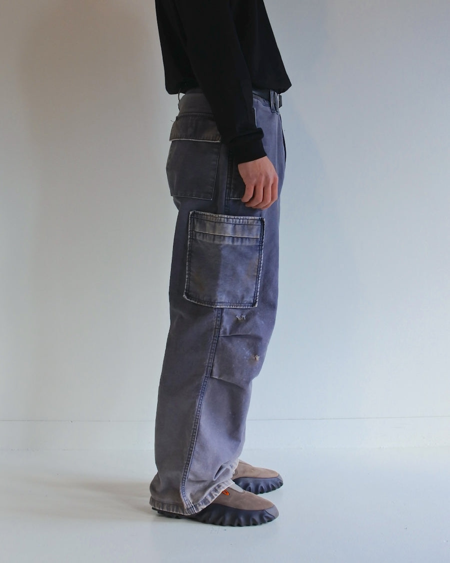 フラップポケットや膝のタック、裾のドローコードなど、ミリタリーのディテールをふんだんに取り入れた一本。内側に配置されることの多いポケットをあえて外側に設けたカーゴポケットが特徴です。ムラ糸で織り上げたバックサテン生地は、ハリとコシのある質感が魅力。さらに、水や薬品の使用を抑えながら生地の凹凸を際立たせる特殊エイジング加工を施し、深みのあるネイビーカラーに仕上げています。