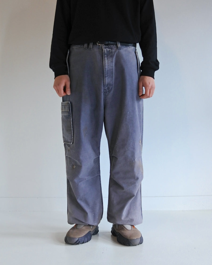 フラップポケットや膝のタック、裾のドローコードなど、ミリタリーのディテールをふんだんに取り入れた一本。内側に配置されることの多いポケットをあえて外側に設けたカーゴポケットが特徴です。ムラ糸で織り上げたバックサテン生地は、ハリとコシのある質感が魅力。さらに、水や薬品の使用を抑えながら生地の凹凸を際立たせる特殊エイジング加工を施し、深みのあるネイビーカラーに仕上げています。