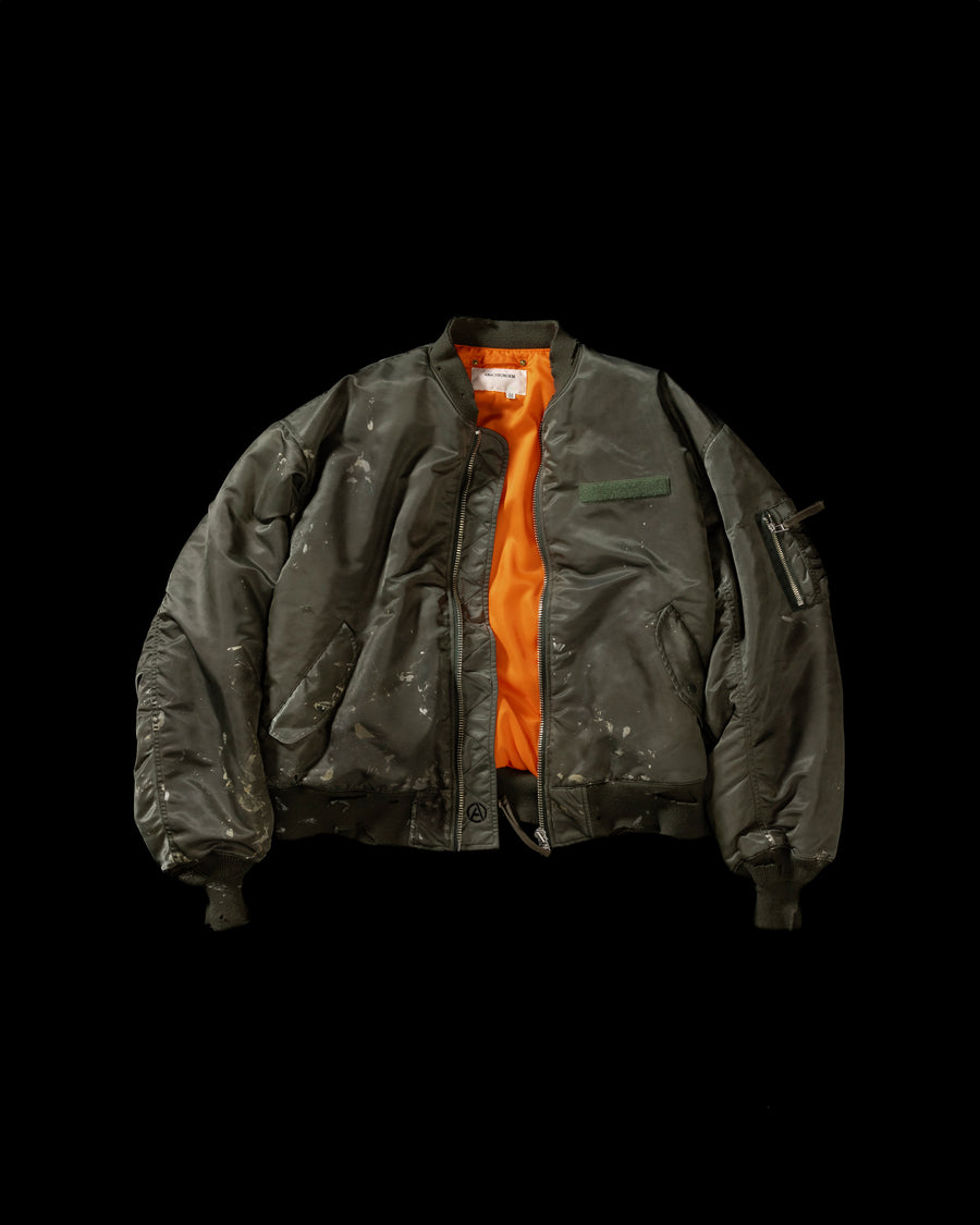 忠実なディテールを保ちながら、シルエットを現代的に整えたMA-1ジャケット。加工によりヴィンテージの風合いを再現した一着です。肉厚でミリタリーらしいツイル生地を使用し、打ち込みの密度や肌触りまでビンテージMA-1に近い仕上がりに。さらに、ダートペイントや特殊吹き付け、ダメージ加工を重ね、洗いをかけて染料を自然に剥がすことで、深みのある表情を生み出しています。カラーはオリーブ。