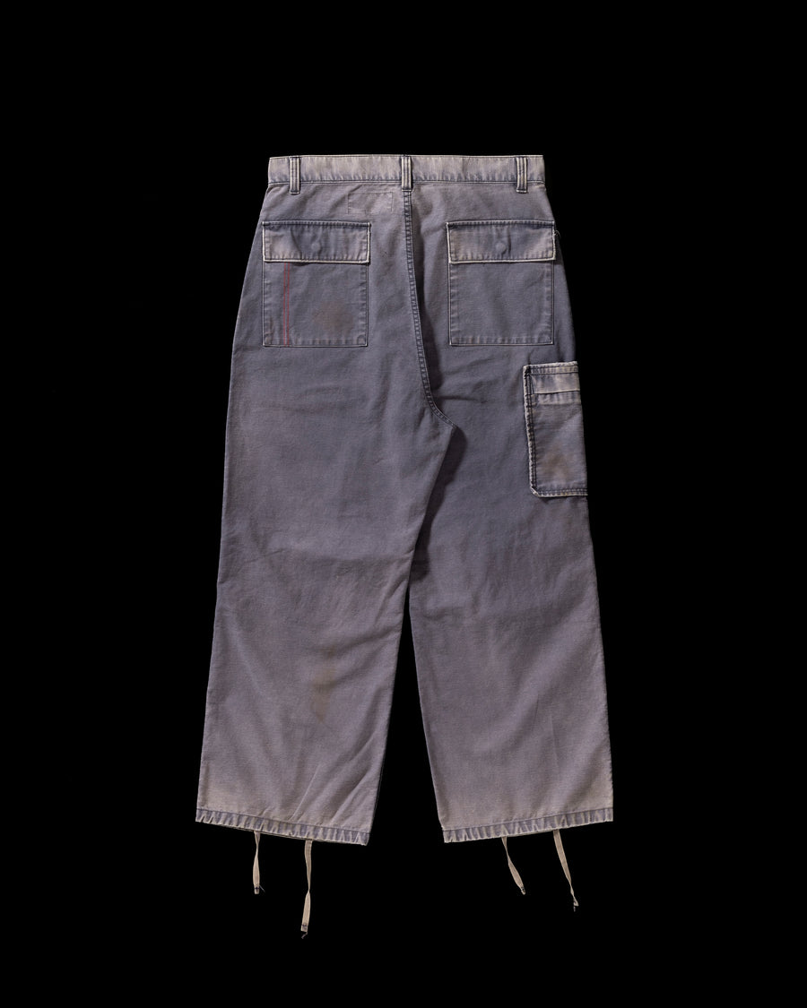 フラップポケットや膝のタック、裾のドローコードなど、ミリタリーのディテールをふんだんに取り入れた一本。内側に配置されることの多いポケットをあえて外側に設けたカーゴポケットが特徴です。ムラ糸で織り上げたバックサテン生地は、ハリとコシのある質感が魅力。さらに、水や薬品の使用を抑えながら生地の凹凸を際立たせる特殊エイジング加工を施し、深みのあるネイビーカラーに仕上げています。
