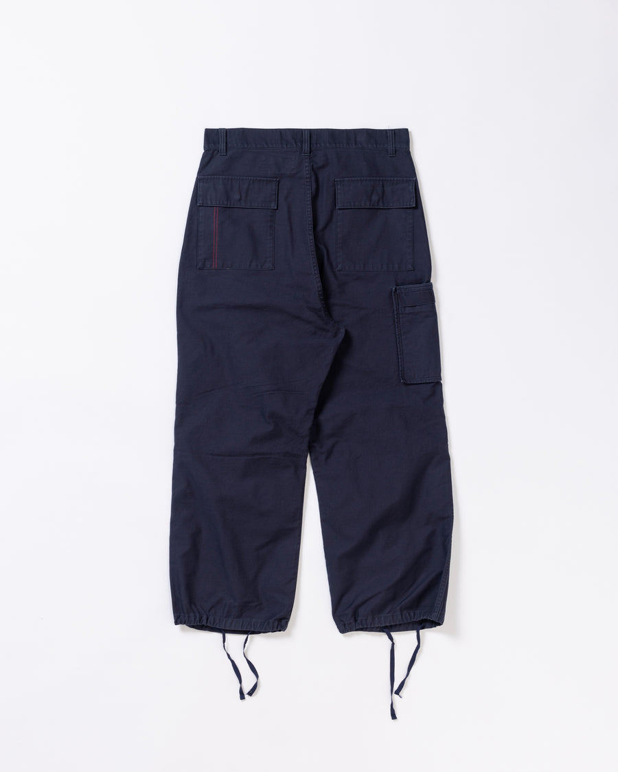 フラップポケットや膝のタック、裾のドローコードなど、ミリタリーディテールを随所に取り入れた1本。通常は内側に配置されるポケットをあえて外側に設けたカーゴポケットが印象的です。ムラ糸で織り上げたバックサテン生地は、独特のハリとコシを持ち、深みのあるネイビーカラーが魅力です。