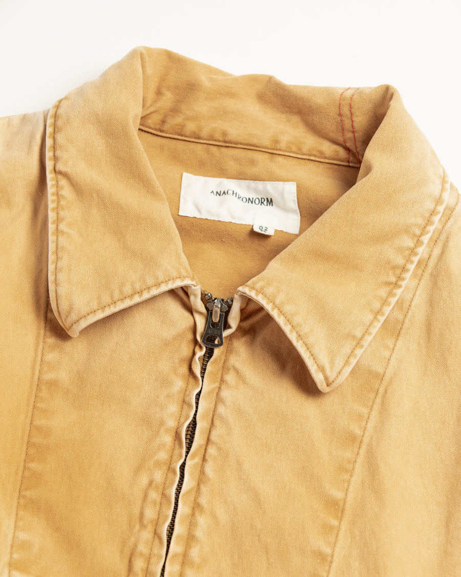 シルエットはゆとりのある身幅とややクロップド丈で設計しており、イエローカラーの鮮やかなトーンがレイヤードスタイルをより引き立てます。インナーアイテムとの重ね着がしやすいバランスに仕上げています。
生地には頒布の中で最も薄手の11号帆布を採用しており、強度・耐久性に優れるだけでなく、着用を重ねるごとにアタリなどの経年変化を楽しめる素材です。また、特殊エイジング加工を施すことで、水や薬品の使用量を抑えながら生地の凹凸が強調され、イエローの色味に自然なフェード感を加えています。