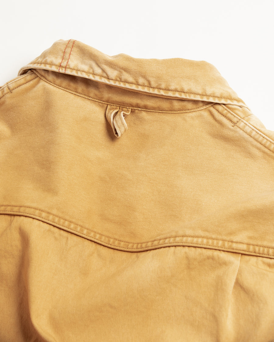 シルエットはゆとりのある身幅とややクロップド丈で設計しており、イエローカラーの鮮やかなトーンがレイヤードスタイルをより引き立てます。インナーアイテムとの重ね着がしやすいバランスに仕上げています。
生地には頒布の中で最も薄手の11号帆布を採用しており、強度・耐久性に優れるだけでなく、着用を重ねるごとにアタリなどの経年変化を楽しめる素材です。また、特殊エイジング加工を施すことで、水や薬品の使用量を抑えながら生地の凹凸が強調され、イエローの色味に自然なフェード感を加えています。