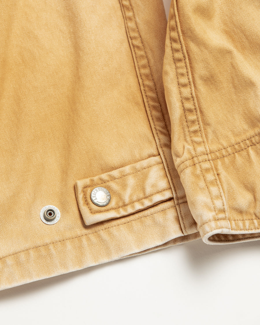 シルエットはゆとりのある身幅とややクロップド丈で設計しており、イエローカラーの鮮やかなトーンがレイヤードスタイルをより引き立てます。インナーアイテムとの重ね着がしやすいバランスに仕上げています。
生地には頒布の中で最も薄手の11号帆布を採用しており、強度・耐久性に優れるだけでなく、着用を重ねるごとにアタリなどの経年変化を楽しめる素材です。また、特殊エイジング加工を施すことで、水や薬品の使用量を抑えながら生地の凹凸が強調され、イエローの色味に自然なフェード感を加えています。