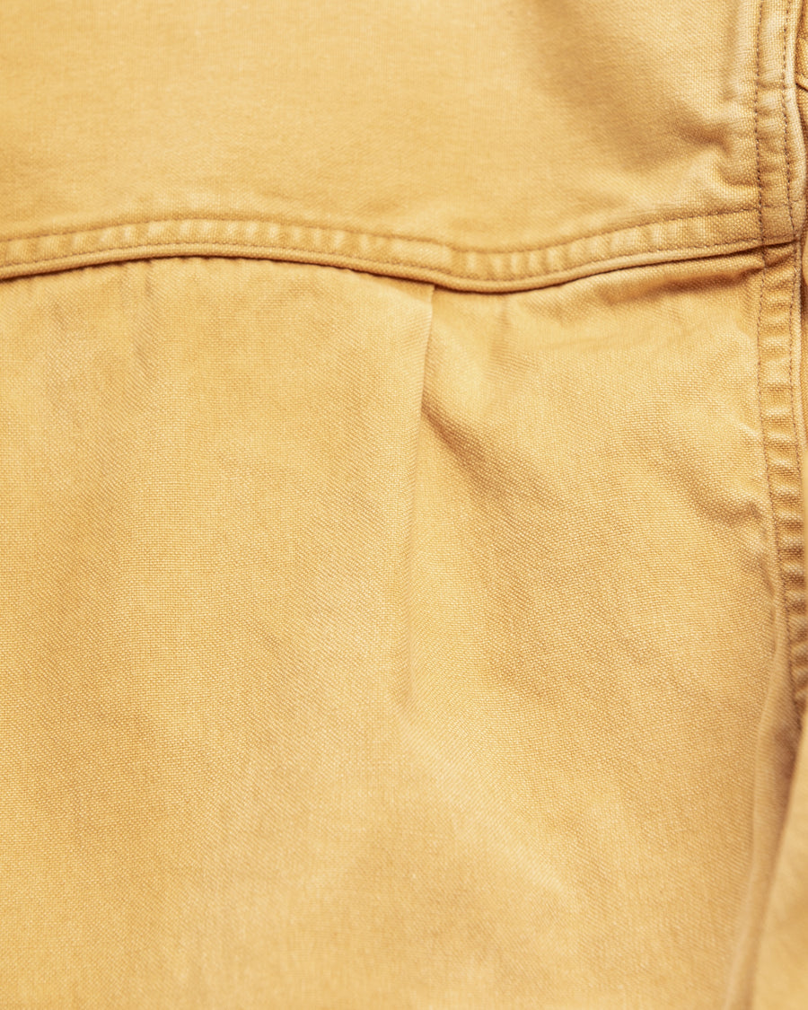 シルエットはゆとりのある身幅とややクロップド丈で設計しており、イエローカラーの鮮やかなトーンがレイヤードスタイルをより引き立てます。インナーアイテムとの重ね着がしやすいバランスに仕上げています。
生地には頒布の中で最も薄手の11号帆布を採用しており、強度・耐久性に優れるだけでなく、着用を重ねるごとにアタリなどの経年変化を楽しめる素材です。また、特殊エイジング加工を施すことで、水や薬品の使用量を抑えながら生地の凹凸が強調され、イエローの色味に自然なフェード感を加えています。