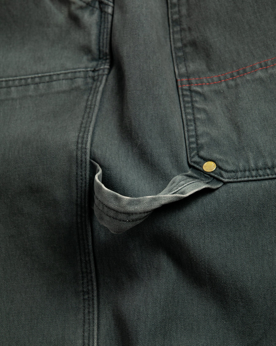 【 商品名：ダブルニーダックペインターパンツ 】

本製品は、レングスをやや長めに設定したブラックカラーのペインターパンツです。ウエスト部分にはナイロンオックス生地で切り替えを施し、ワーク感を抑えた上品なデザインに仕上げています。生地には頒布の中でも最も薄手の11号帆布生地を採用しており、強度・耐久性に優れるとともに、着用を重ねるごとにアタリなどの経年変化を楽しめる素材です。また、水や薬品の使用量を抑えながら生地の凹凸部分のアタリを強調し、同時に自然な脱色感を加える特殊エイジング加工を施しています。