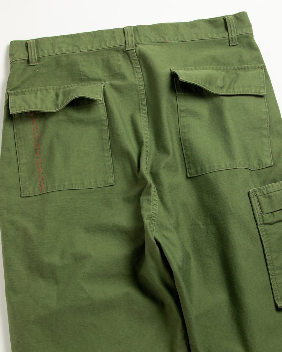 フラップポケットや膝のタック、裾のドローコードなど、ミリタリーディテールを随所に取り入れた1本。通常は内側に配置されるポケットをあえて外側に設けたカーゴポケットが印象的です。ムラ糸で織り上げたバックサテン生地は、独特のハリとコシを持ち、深みのあるオリーブカラーが魅力です。