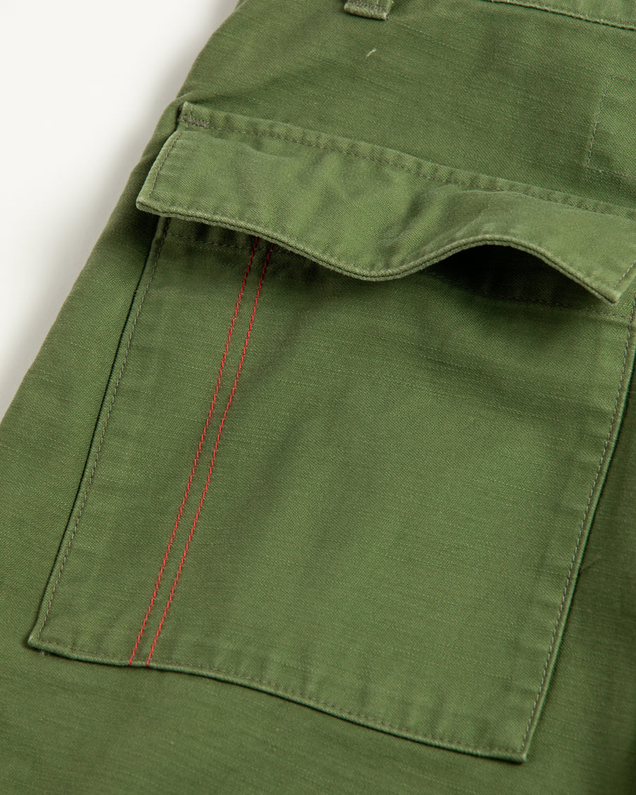 フラップポケットや膝のタック、裾のドローコードなど、ミリタリーディテールを随所に取り入れた1本。通常は内側に配置されるポケットをあえて外側に設けたカーゴポケットが印象的です。ムラ糸で織り上げたバックサテン生地は、独特のハリとコシを持ち、深みのあるオリーブカラーが魅力です。