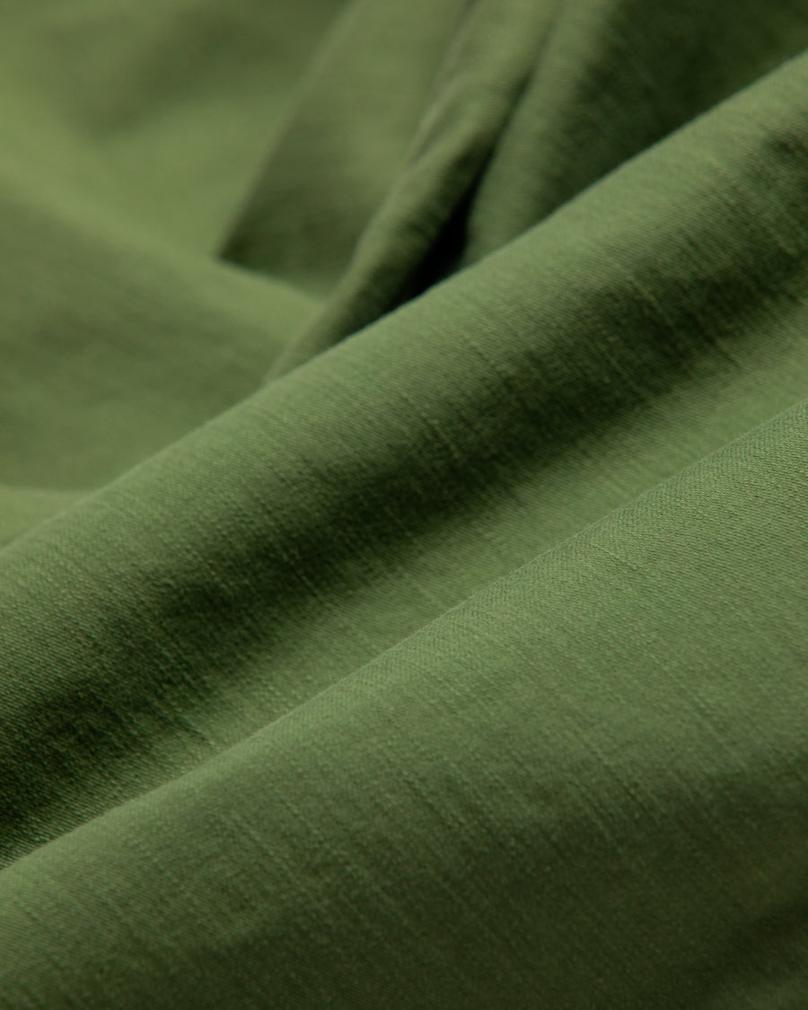 フラップポケットや膝のタック、裾のドローコードなど、ミリタリーディテールを随所に取り入れた1本。通常は内側に配置されるポケットをあえて外側に設けたカーゴポケットが印象的です。ムラ糸で織り上げたバックサテン生地は、独特のハリとコシを持ち、深みのあるオリーブカラーが魅力です。