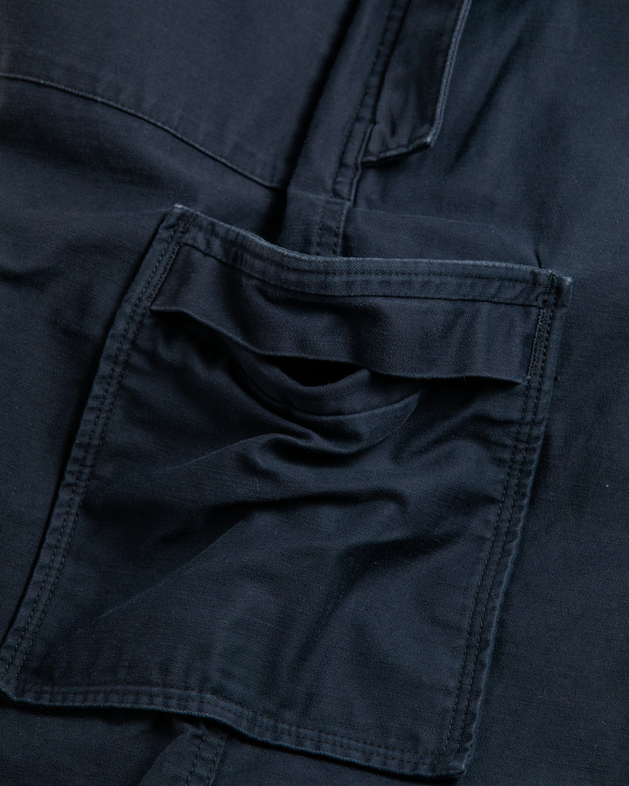フラップポケットや膝のタック、裾のドローコードなど、ミリタリーディテールを随所に取り入れた1本。通常は内側に配置されるポケットをあえて外側に設けたカーゴポケットが印象的です。ムラ糸で織り上げたバックサテン生地は、独特のハリとコシを持ち、深みのあるネイビーカラーが魅力です。