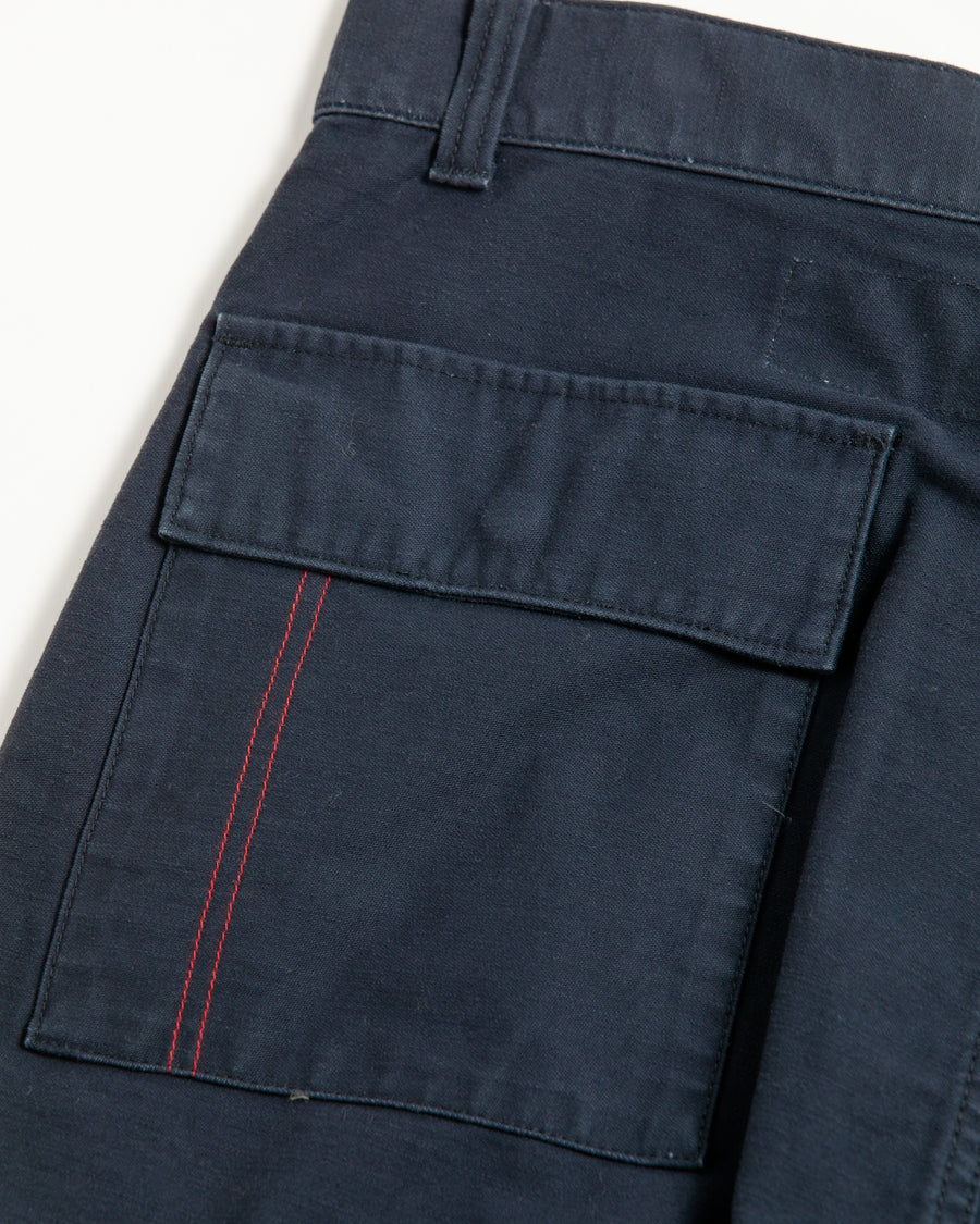フラップポケットや膝のタック、裾のドローコードなど、ミリタリーディテールを随所に取り入れた1本。通常は内側に配置されるポケットをあえて外側に設けたカーゴポケットが印象的です。ムラ糸で織り上げたバックサテン生地は、独特のハリとコシを持ち、深みのあるネイビーカラーが魅力です。