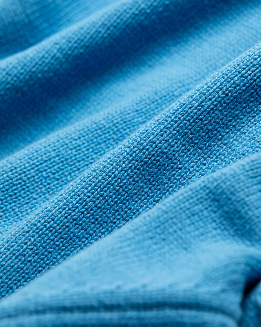 コットンニットを使用したドライバーズニット。
太番手の強撚糸による特殊な天竺編みで、適度なハリと風合いを持たせています。
ゆとりのある身幅ながら、アウターのインナーとしても使いやすいバランスの取れたシルエットに仕上げました。コットン素材のためホームクリーニングも可能です。
カラーは鮮やかなスカイブルー。