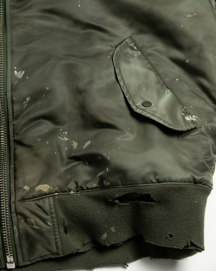 忠実なディテールを保ちながら、シルエットを現代的に整えたMA-1ジャケット。加工によりヴィンテージの風合いを再現した一着です。肉厚でミリタリーらしいツイル生地を使用し、打ち込みの密度や肌触りまでビンテージMA-1に近い仕上がりに。さらに、ダートペイントや特殊吹き付け、ダメージ加工を重ね、洗いをかけて染料を自然に剥がすことで、深みのある表情を生み出しています。カラーはオリーブ。