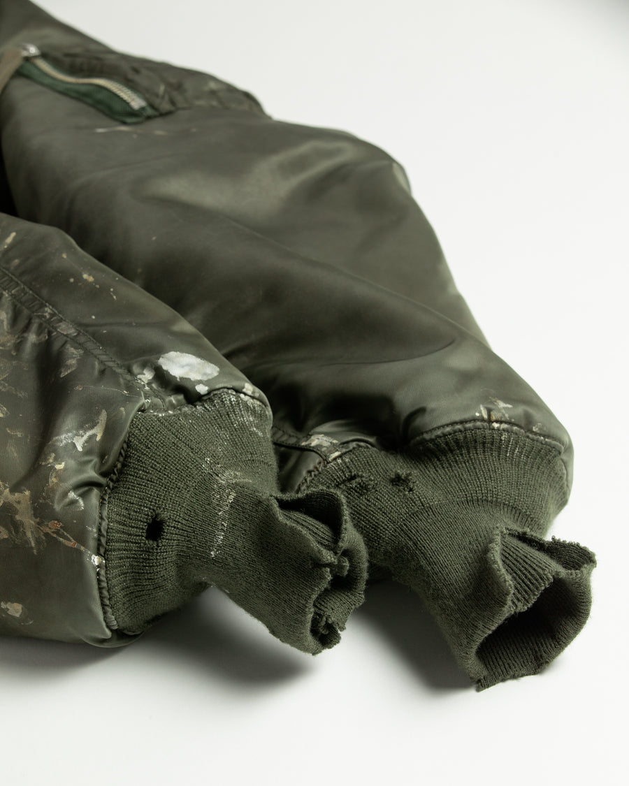 忠実なディテールを保ちながら、シルエットを現代的に整えたMA-1ジャケット。加工によりヴィンテージの風合いを再現した一着です。肉厚でミリタリーらしいツイル生地を使用し、打ち込みの密度や肌触りまでビンテージMA-1に近い仕上がりに。さらに、ダートペイントや特殊吹き付け、ダメージ加工を重ね、洗いをかけて染料を自然に剥がすことで、深みのある表情を生み出しています。カラーはオリーブ。
