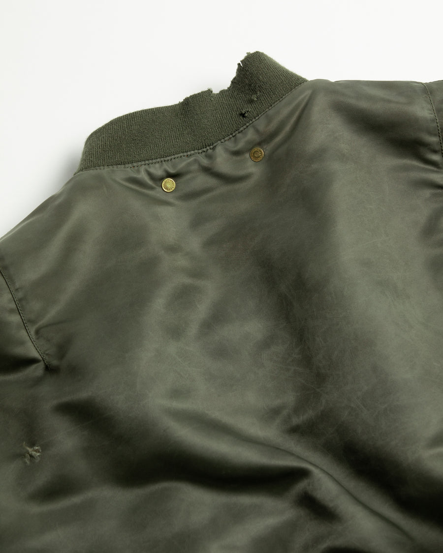 忠実なディテールを保ちながら、シルエットを現代的に整えたMA-1ジャケット。加工によりヴィンテージの風合いを再現した一着です。肉厚でミリタリーらしいツイル生地を使用し、打ち込みの密度や肌触りまでビンテージMA-1に近い仕上がりに。さらに、ダートペイントや特殊吹き付け、ダメージ加工を重ね、洗いをかけて染料を自然に剥がすことで、深みのある表情を生み出しています。カラーはオリーブ。