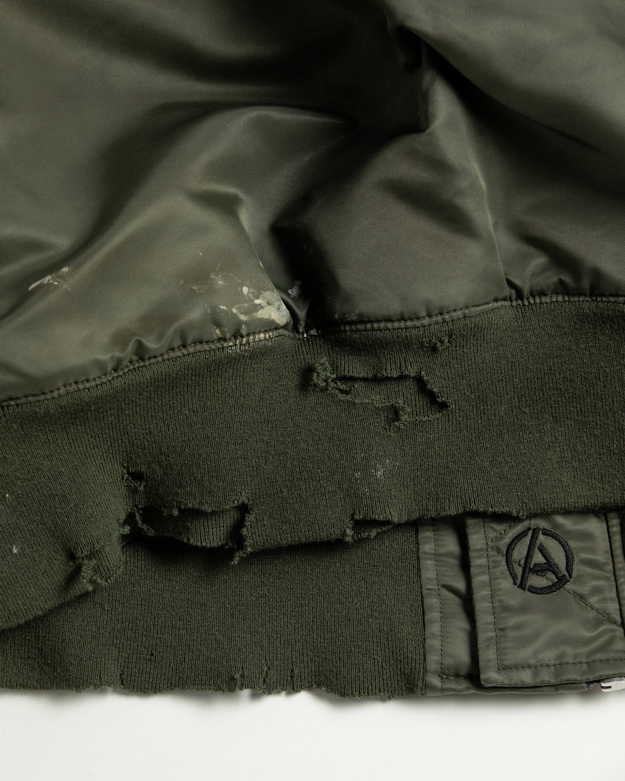 忠実なディテールを保ちながら、シルエットを現代的に整えたMA-1ジャケット。加工によりヴィンテージの風合いを再現した一着です。肉厚でミリタリーらしいツイル生地を使用し、打ち込みの密度や肌触りまでビンテージMA-1に近い仕上がりに。さらに、ダートペイントや特殊吹き付け、ダメージ加工を重ね、洗いをかけて染料を自然に剥がすことで、深みのある表情を生み出しています。カラーはオリーブ。