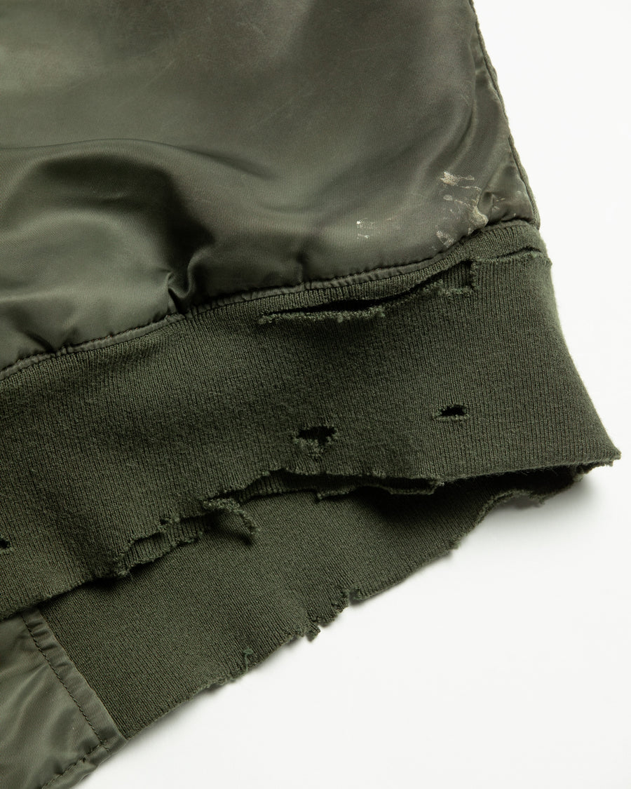 忠実なディテールを保ちながら、シルエットを現代的に整えたMA-1ジャケット。加工によりヴィンテージの風合いを再現した一着です。肉厚でミリタリーらしいツイル生地を使用し、打ち込みの密度や肌触りまでビンテージMA-1に近い仕上がりに。さらに、ダートペイントや特殊吹き付け、ダメージ加工を重ね、洗いをかけて染料を自然に剥がすことで、深みのある表情を生み出しています。カラーはオリーブ。