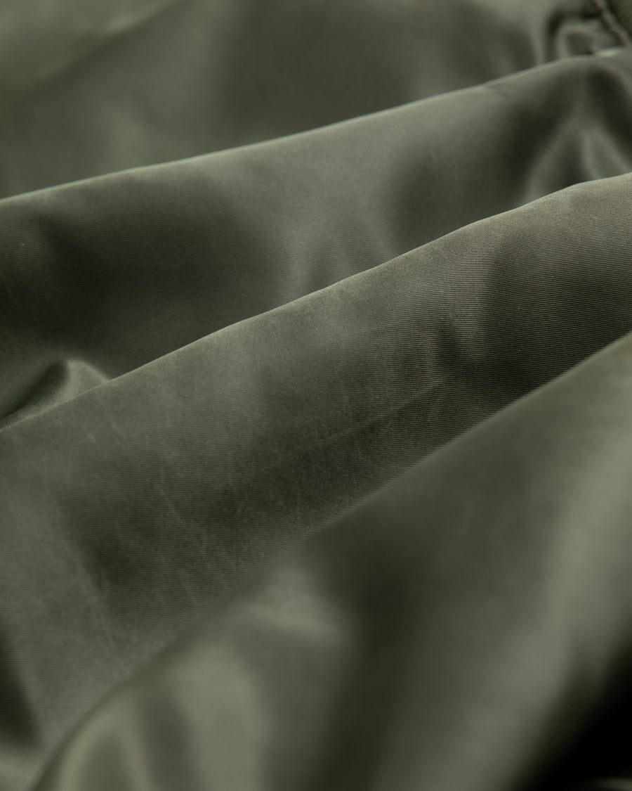 忠実なディテールを保ちながら、シルエットを現代的に整えたMA-1ジャケット。加工によりヴィンテージの風合いを再現した一着です。肉厚でミリタリーらしいツイル生地を使用し、打ち込みの密度や肌触りまでビンテージMA-1に近い仕上がりに。さらに、ダートペイントや特殊吹き付け、ダメージ加工を重ね、洗いをかけて染料を自然に剥がすことで、深みのある表情を生み出しています。カラーはオリーブ。
