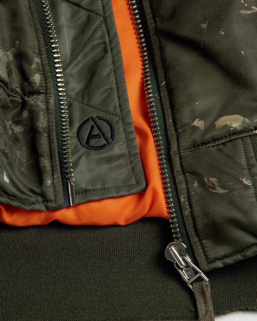 忠実なディテールを保ちながら、シルエットを現代的に整えたMA-1ジャケット。加工によりヴィンテージの風合いを再現した一着です。肉厚でミリタリーらしいツイル生地を使用し、打ち込みの密度や肌触りまでビンテージMA-1に近い仕上がりに。さらに、ダートペイントや特殊吹き付け、ダメージ加工を重ね、洗いをかけて染料を自然に剥がすことで、深みのある表情を生み出しています。カラーはオリーブ。