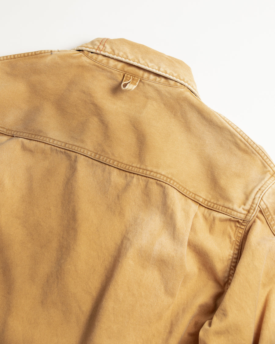 【 商品名：リメイクデトロイトダックジャケット 】

本製品は、ゆとりのある身幅とややクロップド丈に設計されたイエローカラーのジャケットで、インナーアイテムとのレイヤードを楽しめるバランスの良いシルエットが特徴です。生地には頒布の中でも最も薄手の11号帆布生地を使用しており、強度・耐久性に優れるとともに、着用を重ねるごとにアタリなどの経年変化を味わえる素材です。さらに、水や薬品の使用量を抑えながら生地の凹凸部分のアタリを強調し、同時に自然な脱色感を生み出す特殊エイジング加工を施し、加えてサンフェードによるダメージ加工も行うことで、より深みのある表情に仕上げています。